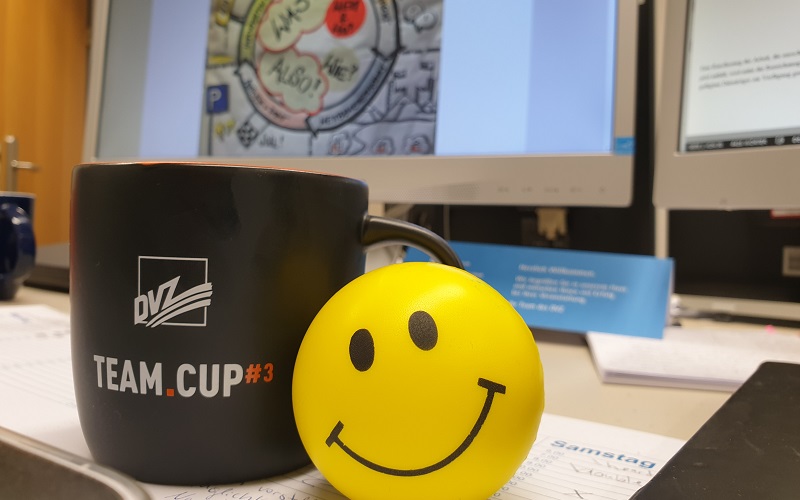 Eine DVZ-Tasse und ein gelber Ball mit einem Smiley-Gesicht liegen auf einem Bürotisch