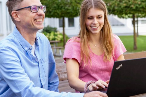 Zwei DVZ-Mitarbeiter*innen sitzen an einem Laptop und lächeln