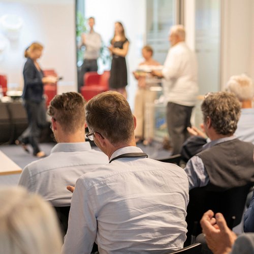 Mehrere DVZ-Mitarbeiter*innen hören einem Meeting zu