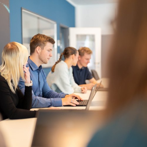 Gruppe von Auszuildenden und dual Studierenden sitzt an ihren Laptops