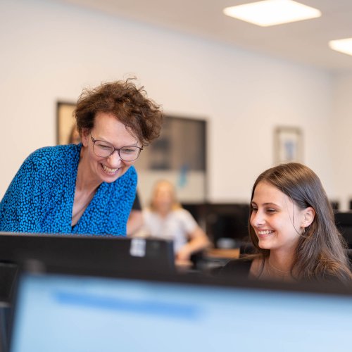 zwei Frauen schauen gemeinsam auf einen Computer und lächeln